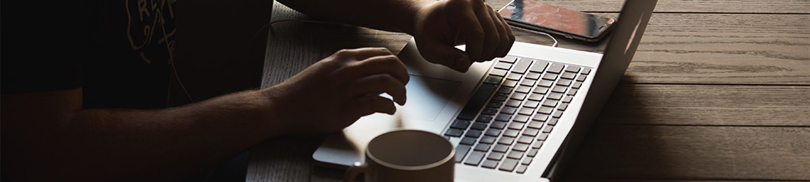 Person typing on a laptop having coffee.